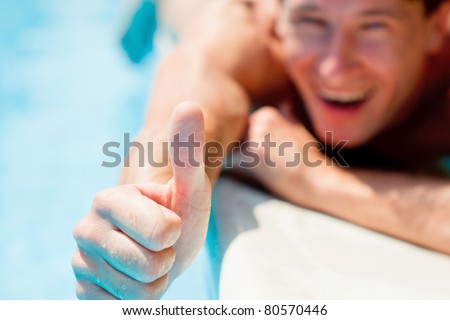 Young man smiling and showing thumb up under the summer sun near swimming pool