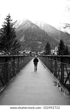 black and white image of a lady walking alone on steel bridge with mountain background