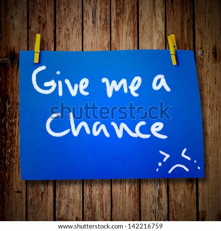 note paper and clothes peg on a wooden background with give me a chance message