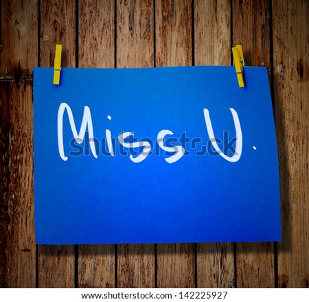note paper and clothes peg on a wooden background with message Miss you