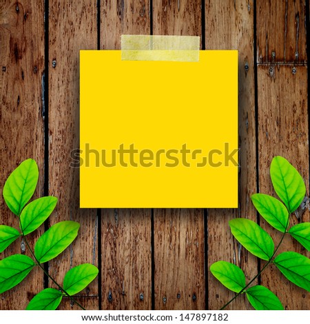 Yellow paper note and green leaves on the old wooden background