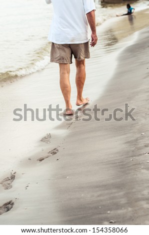 Beach travel - man walking on sand beach leaving footprints in the sand. Closeup detail of male feet