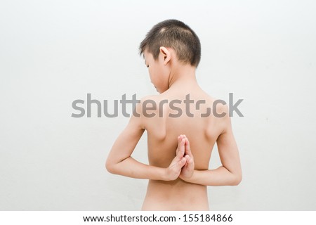 young boy doing yoga exercise in Virasana or Hero Pose with reversed prayer or namaste in studio against a mottled background from behind.