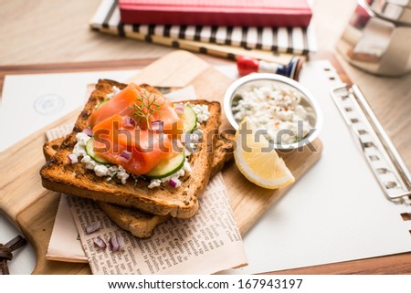 smoked salmon with cucumber over toast decorated with old newspaper coffee and notebook.