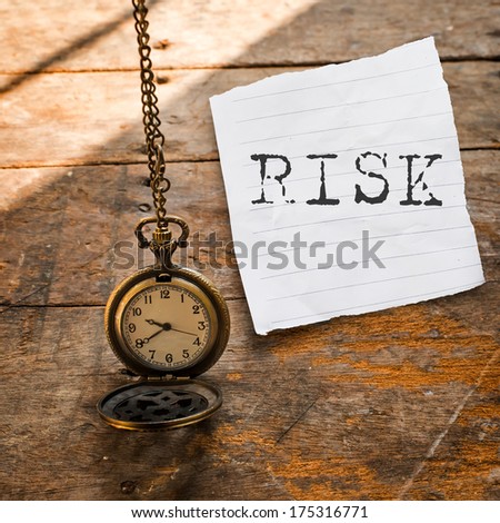 Risk message on Vintage pocket watch on chain and torn paper on wooden background