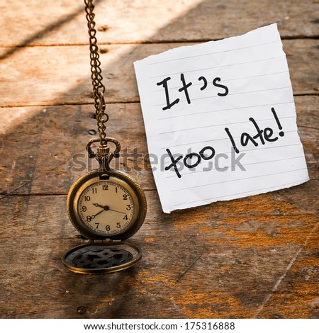 Ti\'s too late message on Vintage pocket watch on chain and torn paper on wooden background