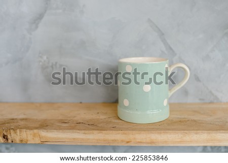 Pastel Green cup with dot on wooden background and cement wall.