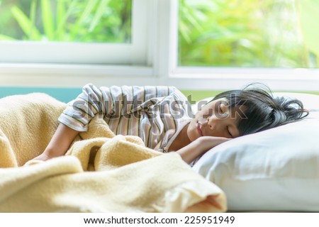 Asian girl sleeping on bed covered with blanket.