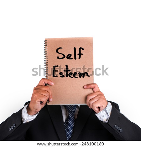 Business man standing and hidden his face with self esteem note on brown notebook