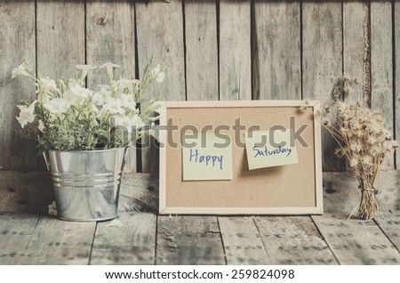 Vintage style effect Happy Saturday message on corkboard with flowers  by wooden background