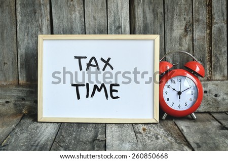 Tax time message note on white board with red retro clock on wooden background.