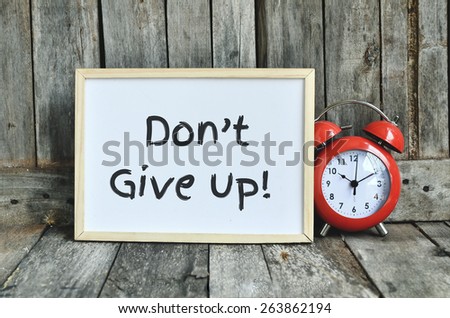 Don\'t give up  message note on white board with red retro clock on wooden background.