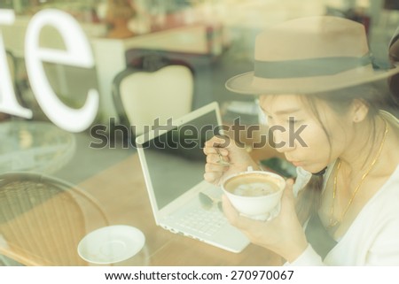 Asian woman drinking coffee and using computer in cafe. Photo filter effect. Selective focused