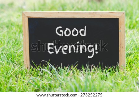 Good evening message on blackboard on green grass.