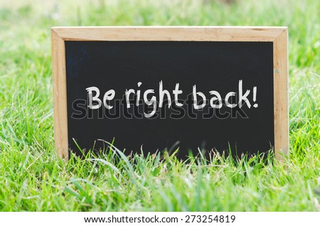 Be right back message on blackboard on green grass.