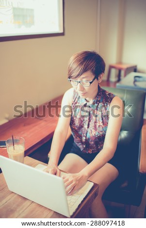 Asian woman drinking coffee and using computer in cafe. Photo filter effect. Selective focused