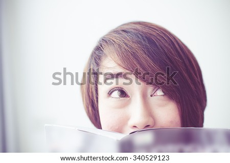 Asian woman rests at the sofa reading book,her eyes looking up something, vintage tone.