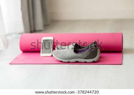 Selective focus close up gray sport shoes and smart phone on pink yoga mat at home, healthy concept.
