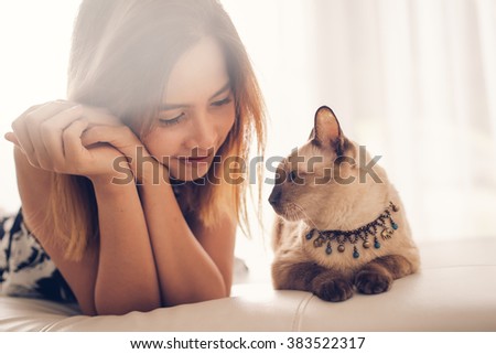 Asian woman and cat laying on sofa with window light.