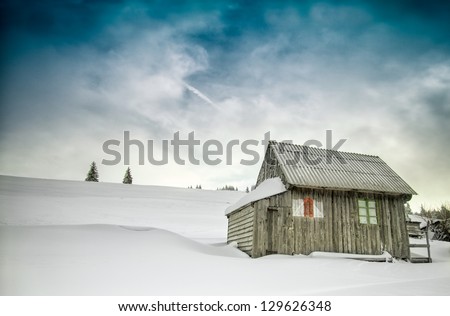 Winter scene in mountains with old house with hand-painted tourist trail sign