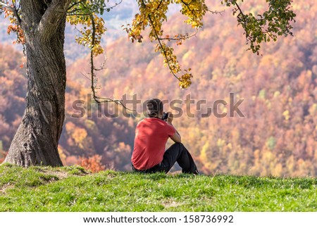 Man taking photos under autumn tree - outdoor relaxing hobby