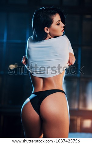 Young sexy woman standing on night window background with warm and cold lights. Focus on buttocks.