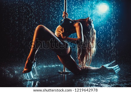 Young sexy slim woman pole dancing in dark interior with smoke and water. Dramatic colors.