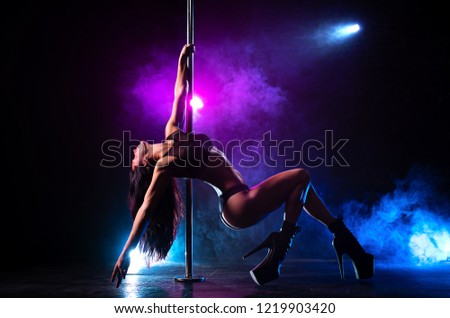 Young sexy slim brunette woman pole dancing in dark interior with smoke and lights