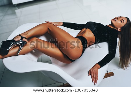 Young slim sexy brunette woman in black clothing lying on white chair