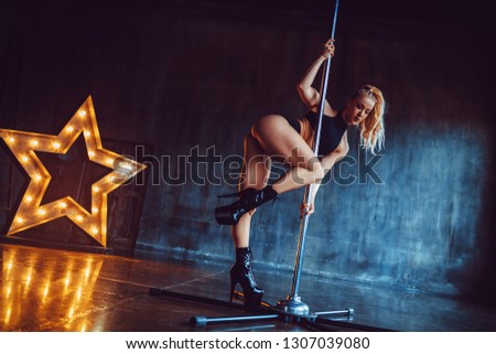 Young sexy pole dancing woman standing in dark stone interior with star lights shape