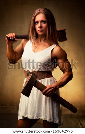 Young woman bodybuilder with hammer and axe. Ancient style.