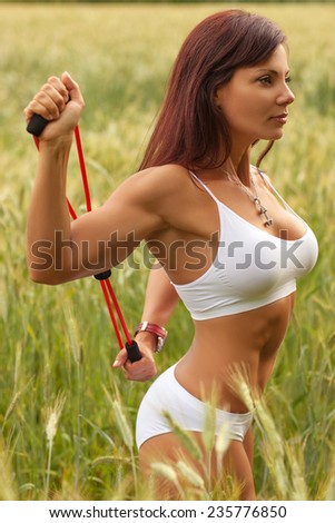 Woman in white clothing sports training with rubber band at summer field.