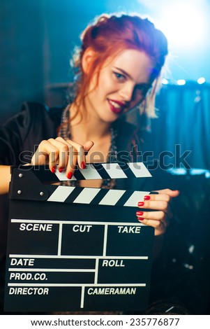 Young woman film director with clapper portrait. Blue light on background. Focus on clapper.
