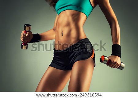 Young sports sexy fitness woman body with dumbbells posing on wall background.