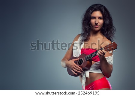 Young sexy brunette woman in red lingerie playing on small guitar. Portrait on wall background.