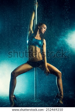 Young slim sexy brunette pole dance woman. Water rain with smoke and flares.