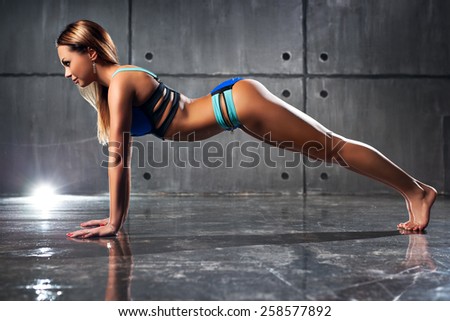 Young sexy slim fitness woman doing push-ups on wall background.
