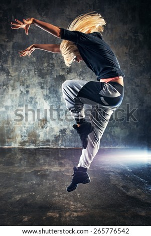 Young woman modern dancer jumping. On dark stone wall background.