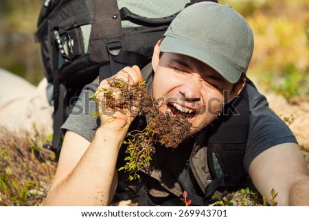 Young hungry man tourist surviving by eating grass and roots in forest.