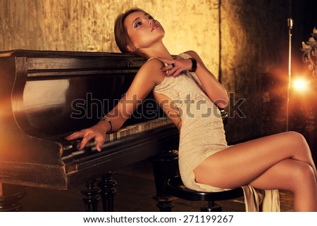 Young elegant woman in dress sitting at piano in retro style interior.