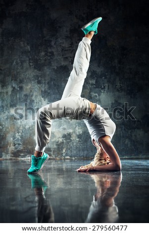 Young woman modern dancer in white. On dark stone wall background.