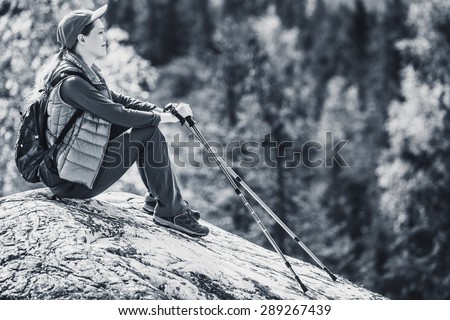 Young woman tourist sitting on mountain top and looking aside on forest. Black and white colors.