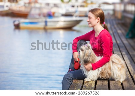 Young woman with shih-tzu dog sitting on town quay with boats.