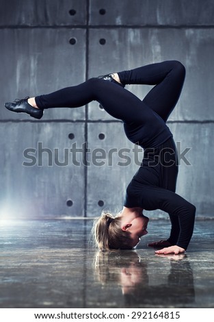 Strong woman gymnast in black clothing stretching upside down on wall background.