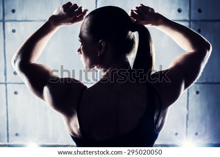 Strong woman bodybuilder back view. Contrast silhouette on wall background.