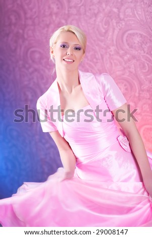 Young blond woman in pink dress dancing. Soft pink and blue background.
