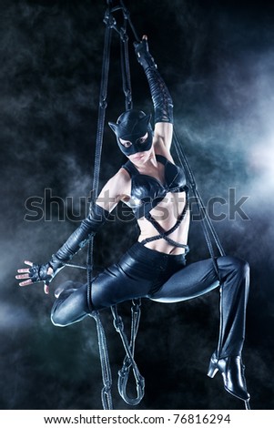 Young woman gymnast in cat suit. On black background with smoke.