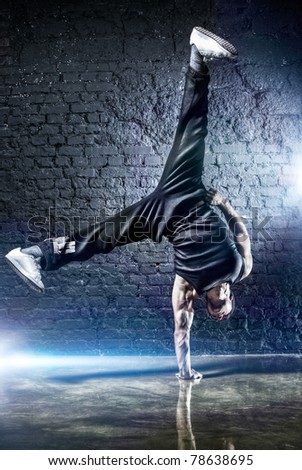 Young strong man break dance. On dark wall background.