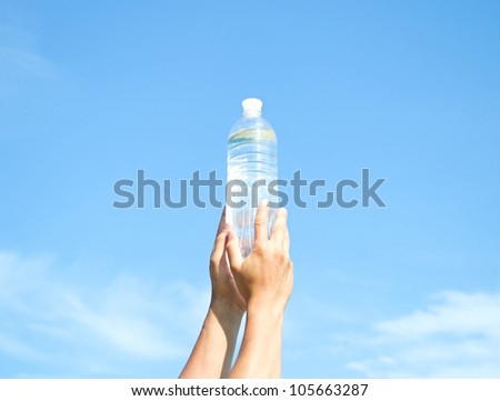 hands with a plastic bottle of water on blue sky background