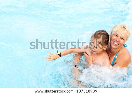 Smiling middle-aged woman and  little girl swimming in a pool with blue water and hydro massage